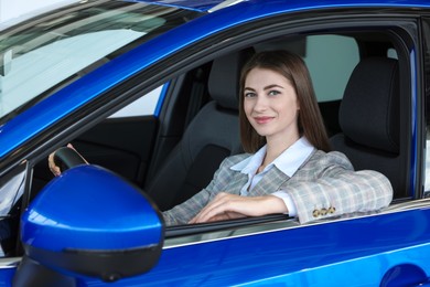 Photo of Young woman inside new blue car in salon