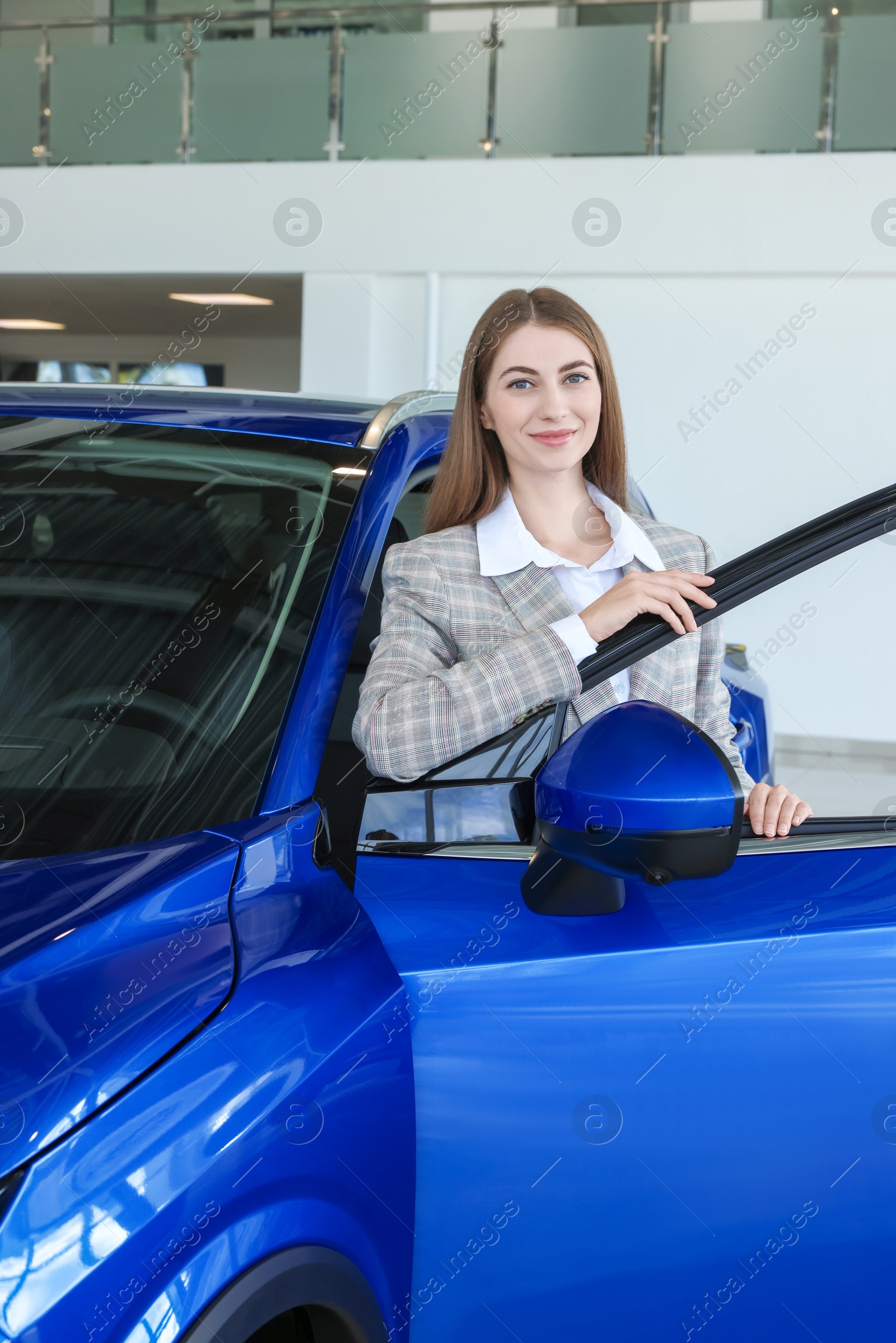 Photo of Young woman near new blue car in salon