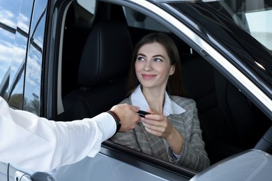 Photo of Salesman giving key to client inside new car in salon