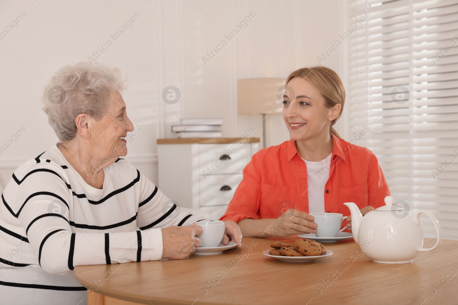 Photo of Caregiver and senior woman enjoying hot drink at table indoors