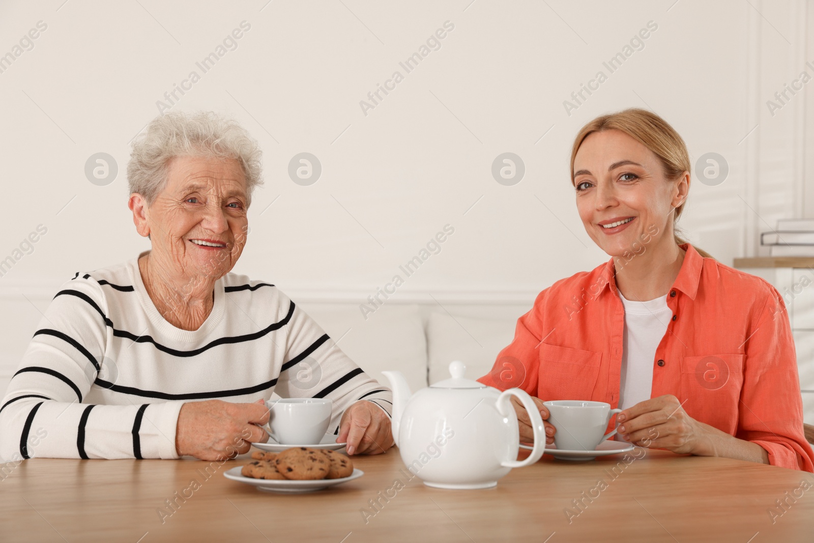 Photo of Caregiver and senior woman enjoying hot drink at table indoors