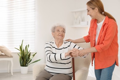 Photo of Caregiver supporting senior woman in living room at home