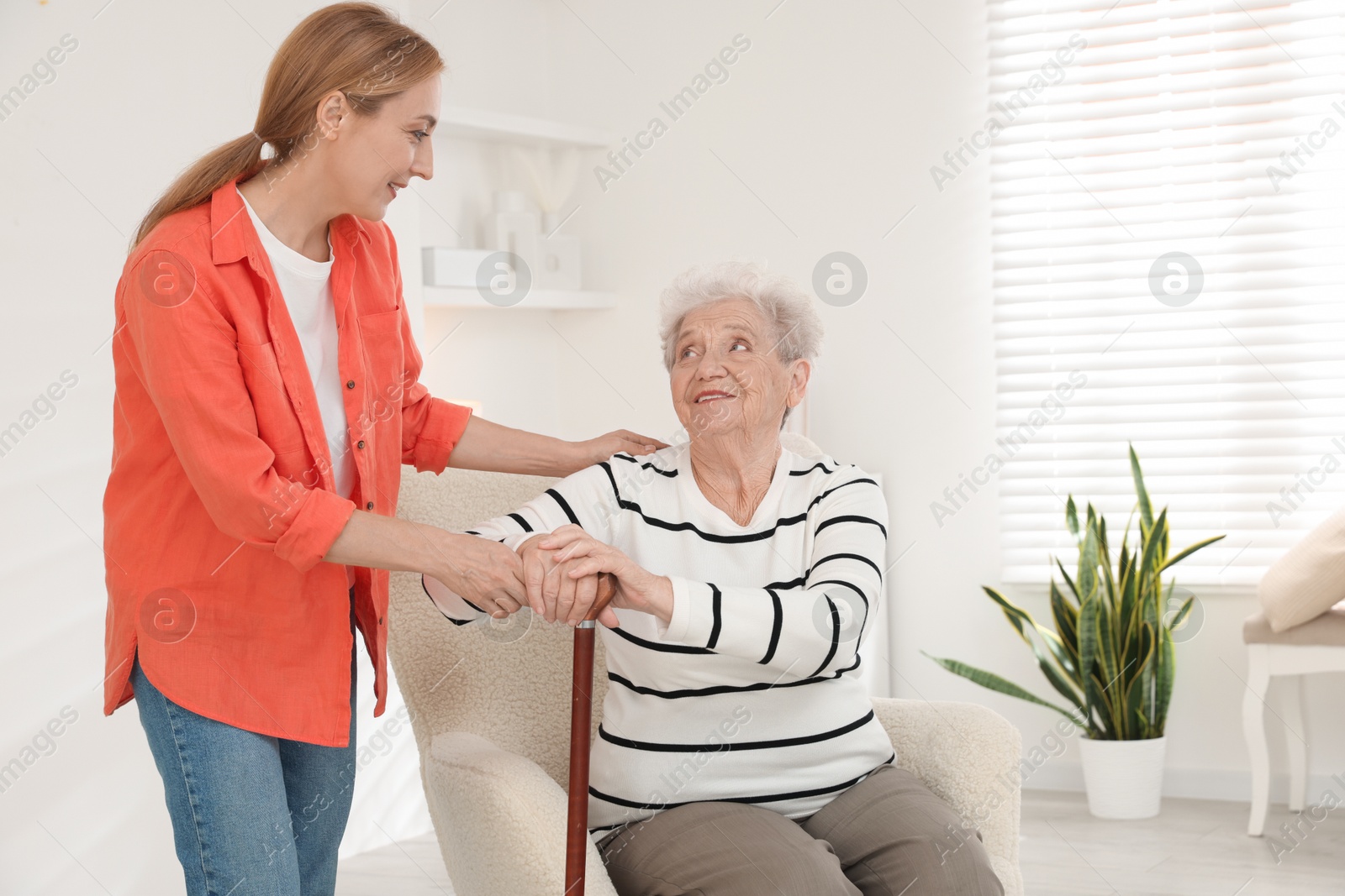 Photo of Caregiver supporting senior woman in living room at home