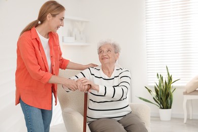 Photo of Caregiver supporting senior woman in living room at home