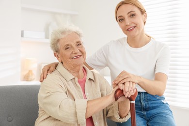 Photo of Caregiver supporting senior woman in living room at home