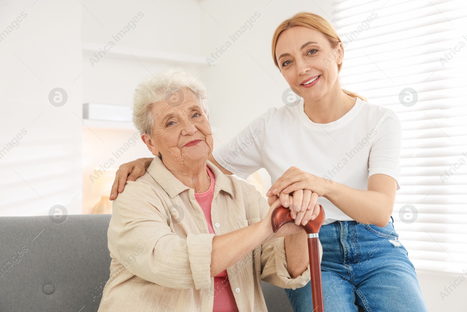 Photo of Caregiver supporting senior woman in living room at home