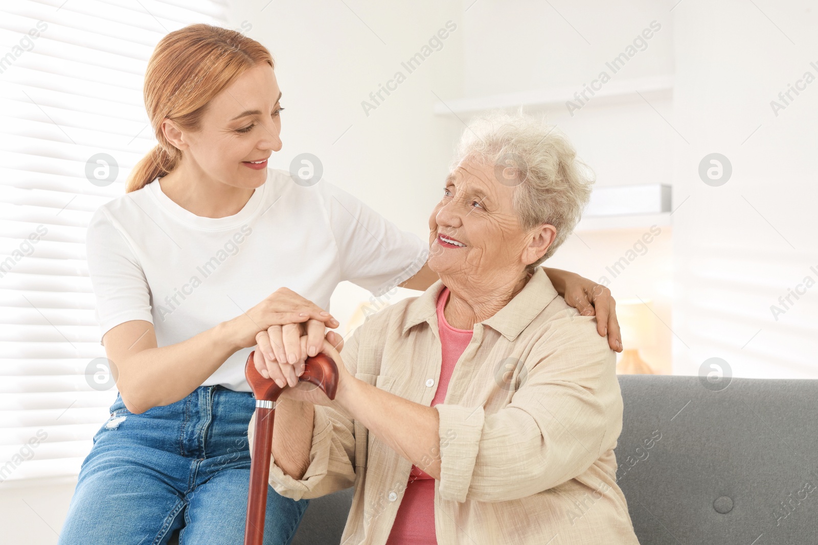 Photo of Caregiver supporting senior woman in living room at home