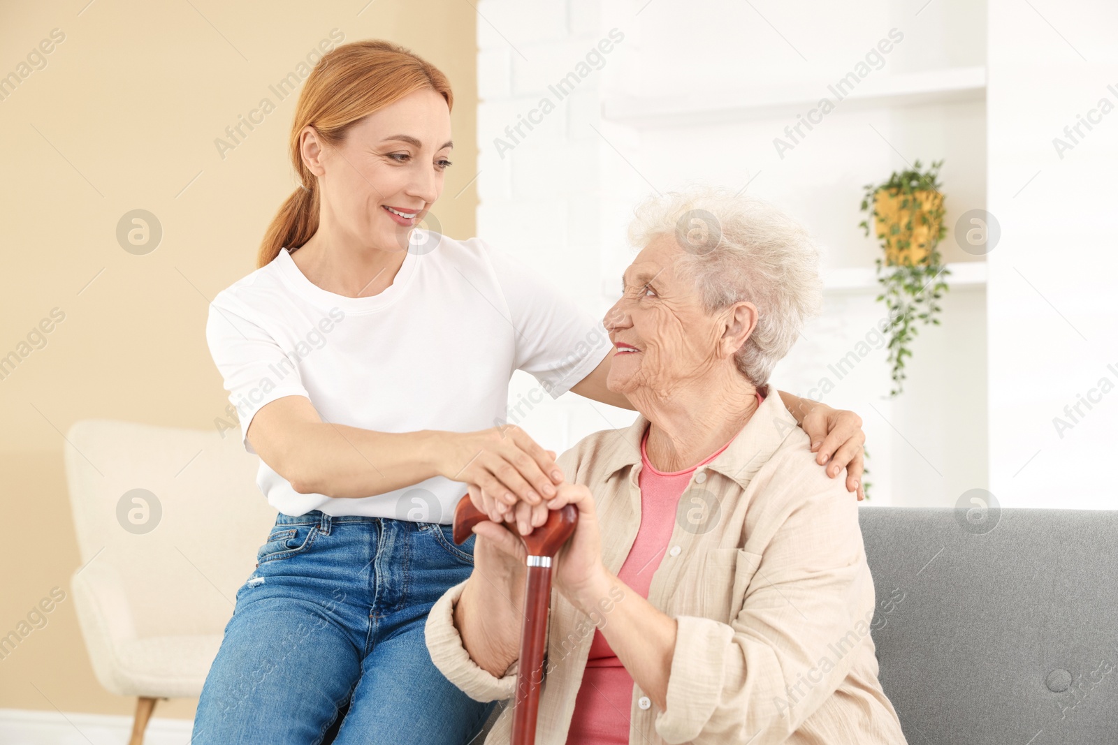 Photo of Caregiver supporting senior woman in living room at home