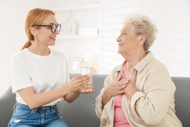 Photo of Caregiver giving glass of water to senior woman at home