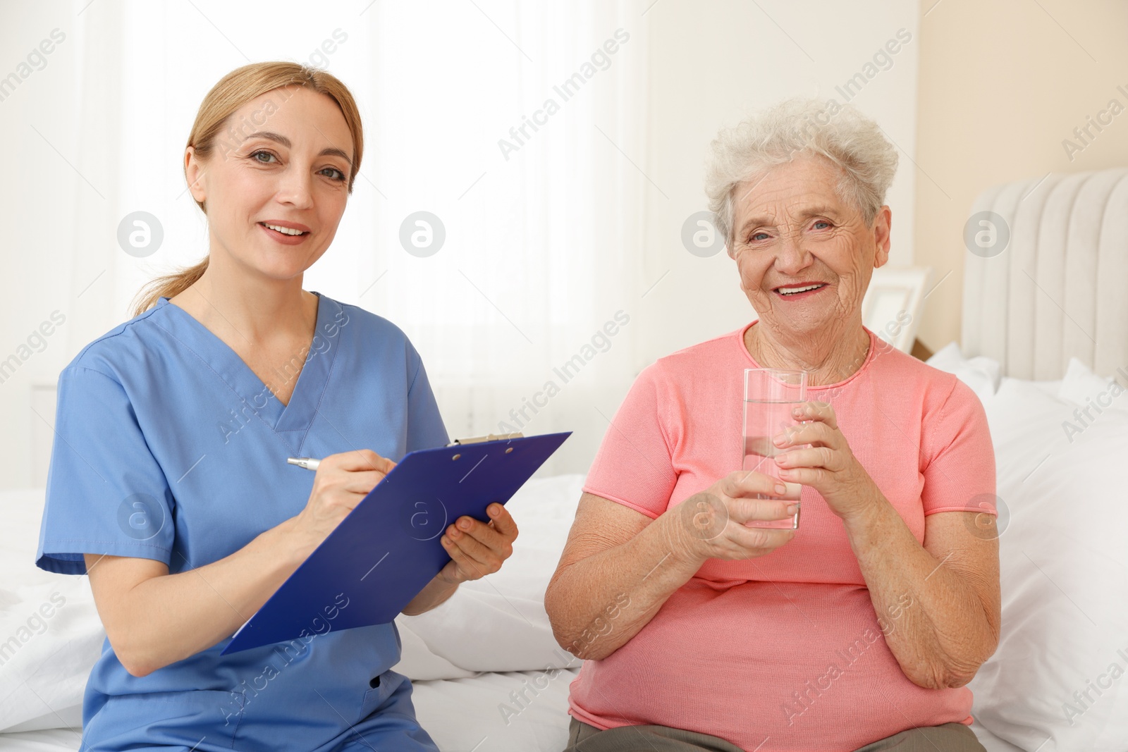 Photo of Healthcare worker with clipboard consulting senior patient on bed indoors