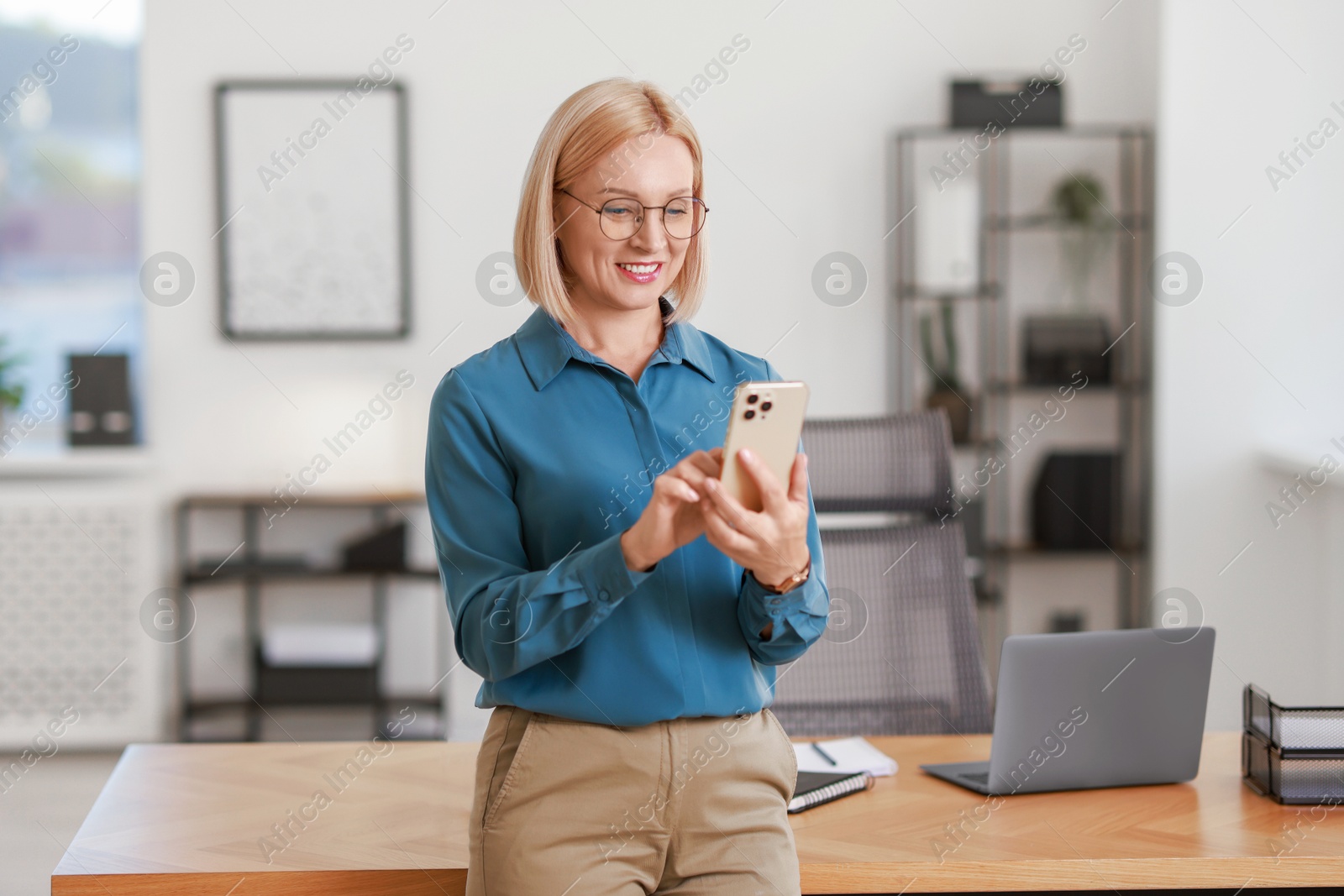 Photo of Smiling middle aged woman using smartphone in office