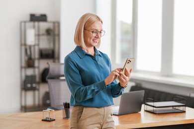 Photo of Smiling middle aged woman using smartphone in office