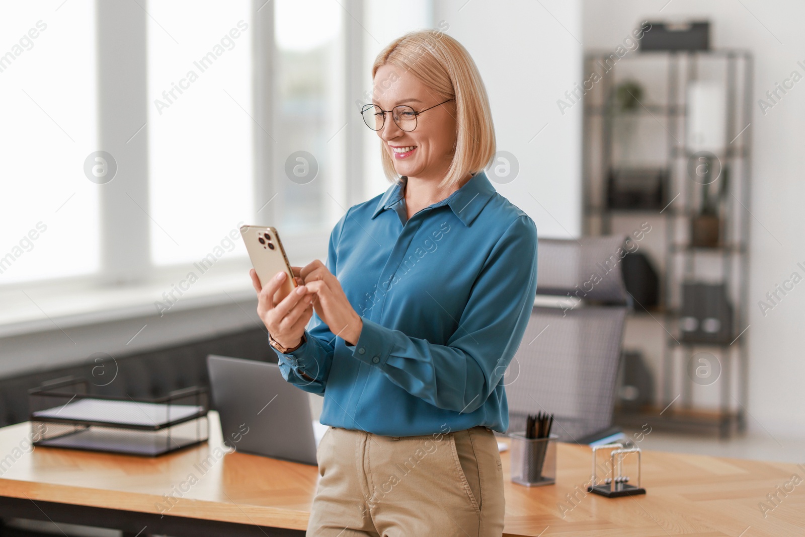 Photo of Smiling middle aged woman using smartphone in office