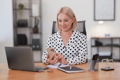 Smiling middle aged woman using smartphone at table in office