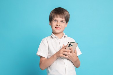 Photo of Cute little boy with smartphone on light blue background