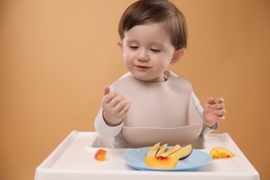 Photo of Healthy baby food. Cute little kid eating fruits in high chair on beige background