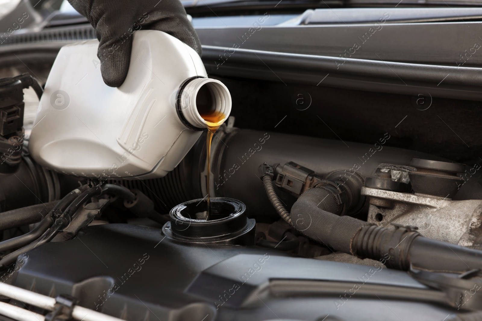 Photo of Man pouring motor oil into car engine, closeup