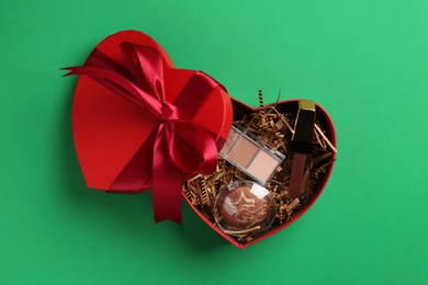 Photo of Christmas gift box with decorative cosmetics on green background, top view