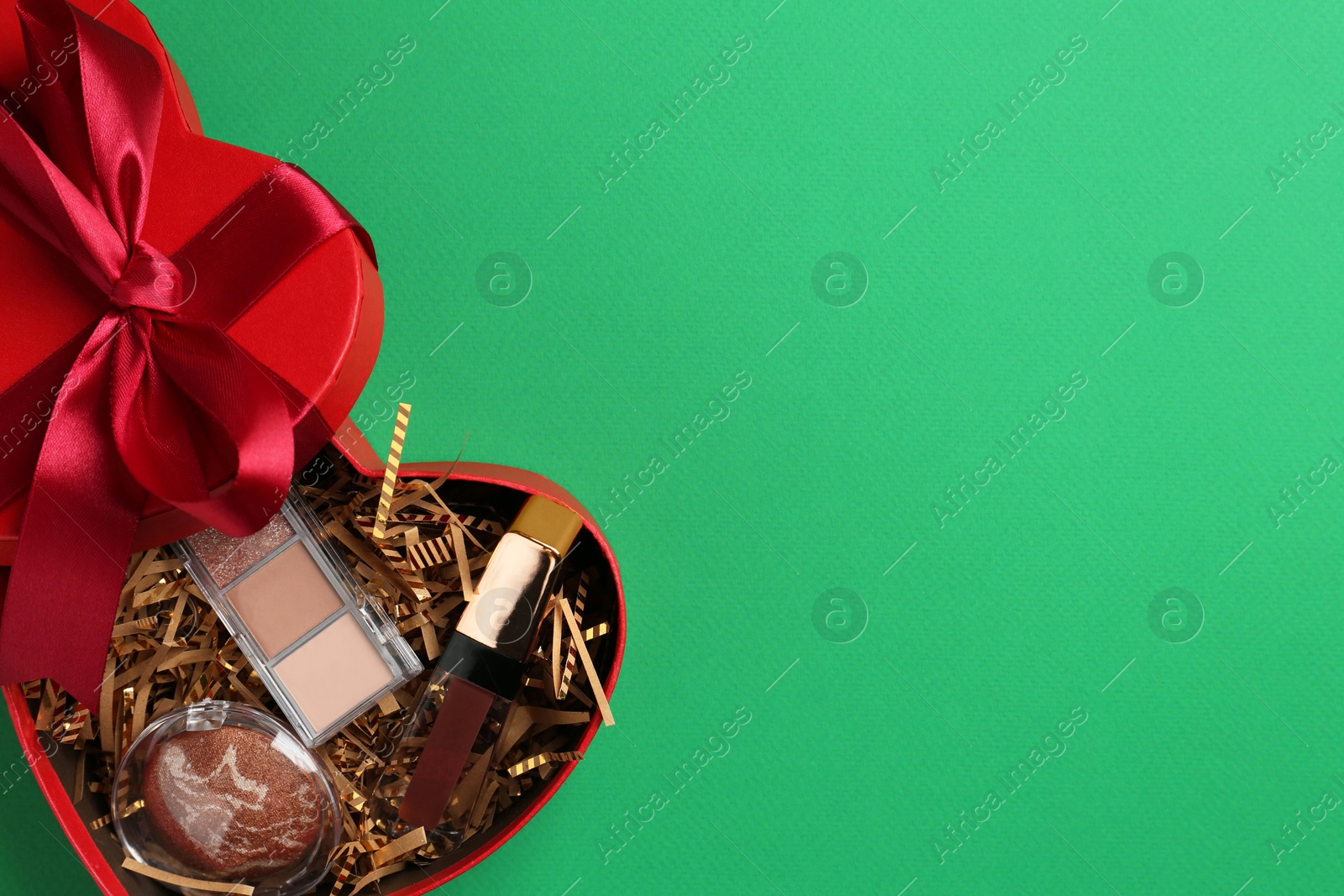 Photo of Christmas gift box with decorative cosmetics on green background, top view. Space for text