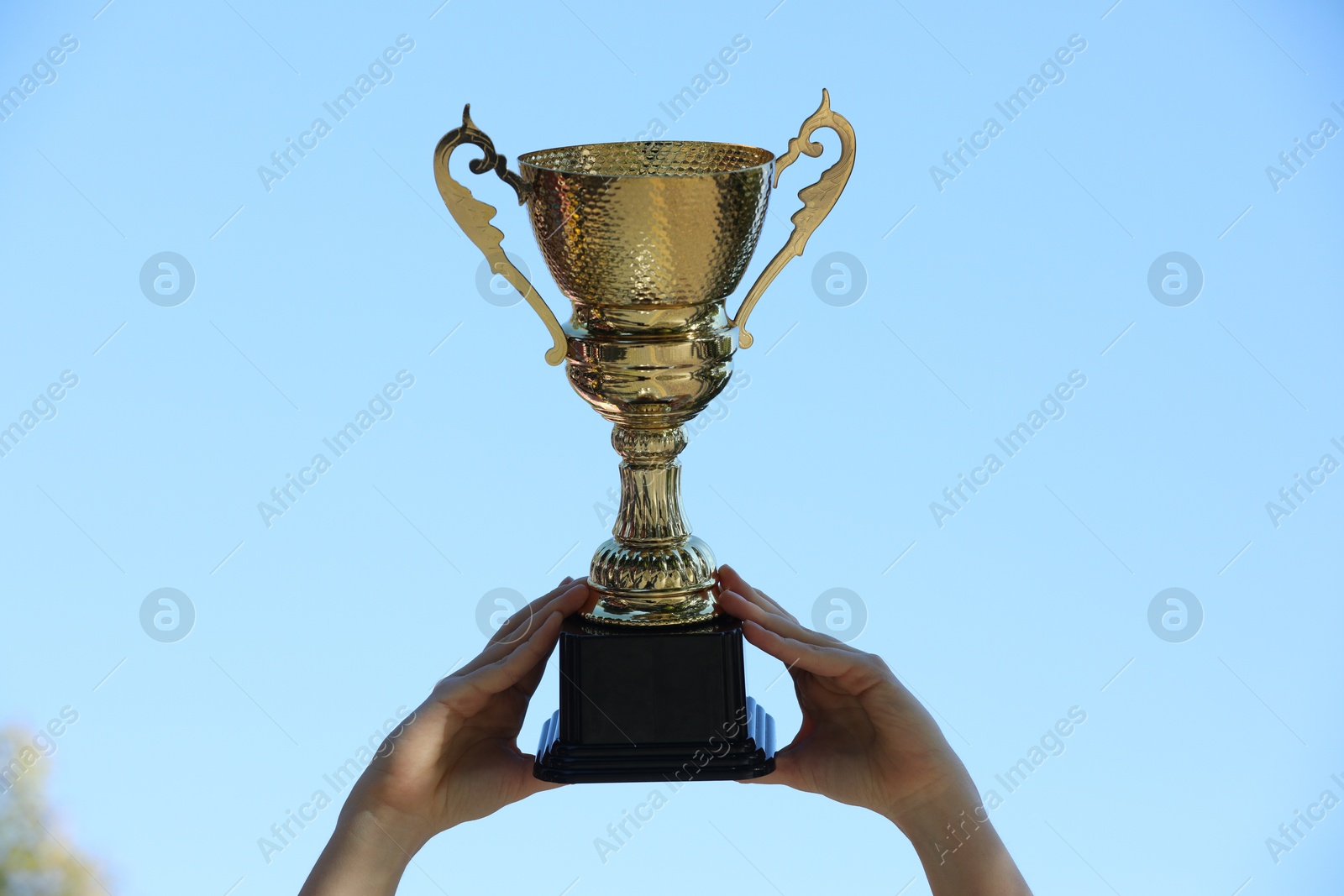 Photo of Woman holding golden trophy against blue sky outdoors, closeup