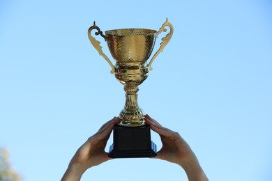 Woman holding golden trophy against blue sky outdoors, closeup