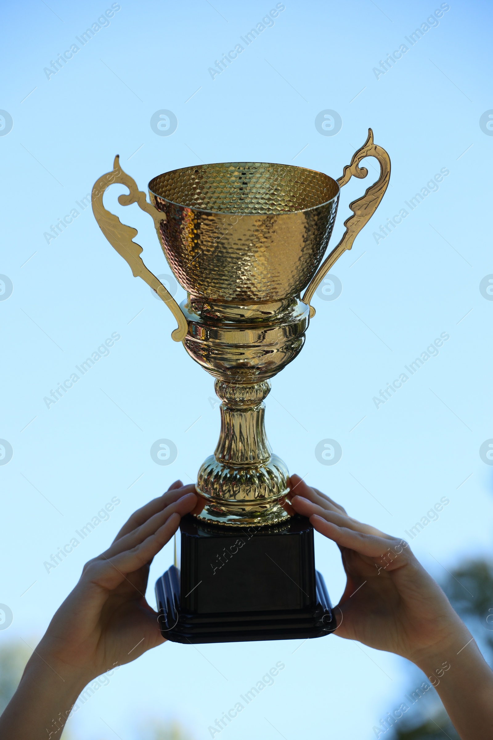 Photo of Woman holding golden trophy against blue sky outdoors, closeup