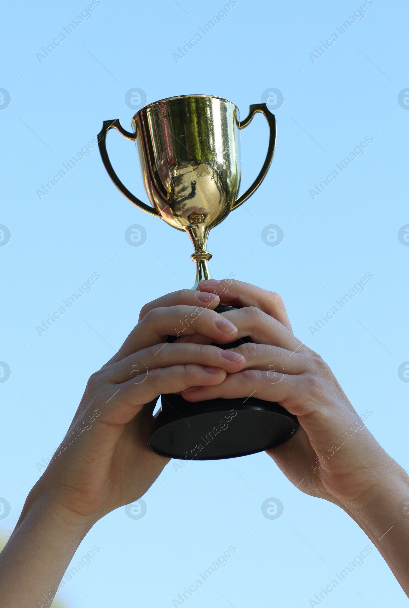 Photo of Woman holding golden trophy against blue sky outdoors, closeup