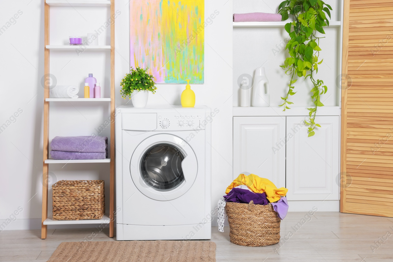 Photo of Washing machine, detergents, clean towels and basket with laundry in room