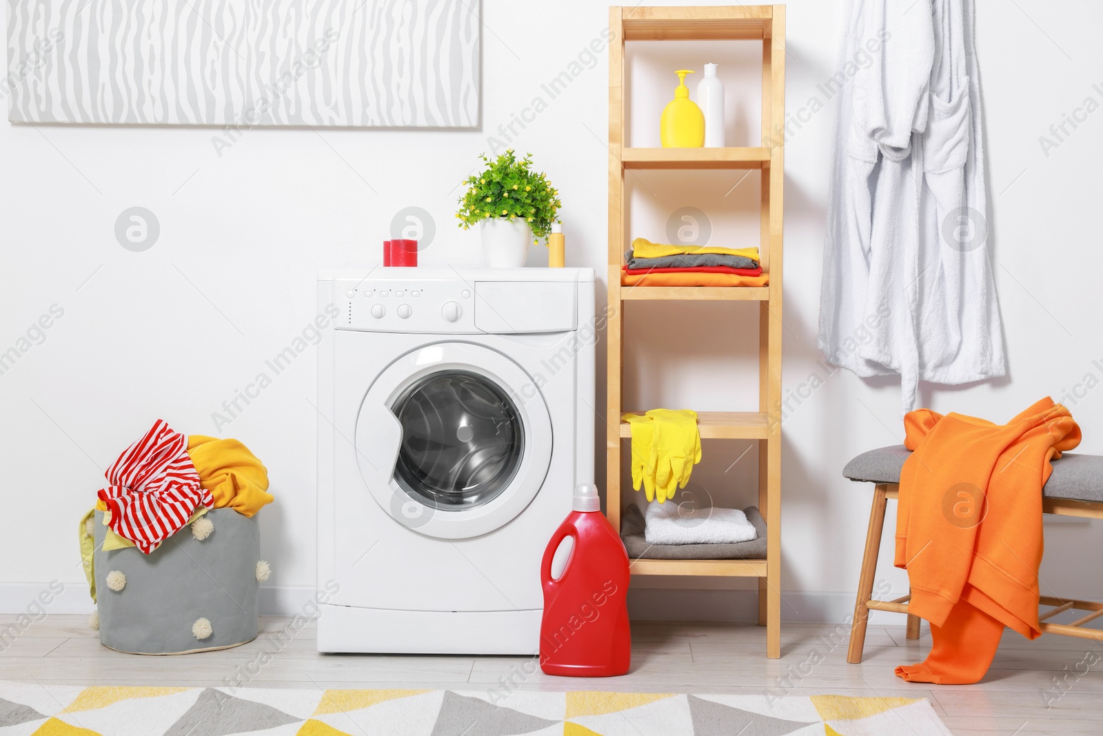 Photo of Washing machine, detergents, bathrobe and basket with laundry in room