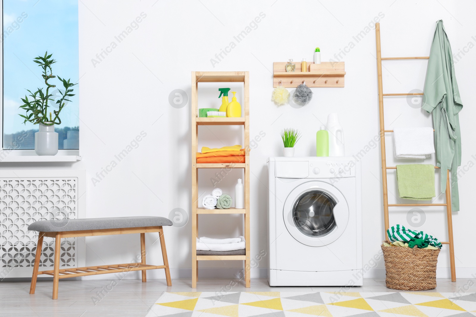 Photo of Washing machine, detergents, bathrobe and basket with laundry in room