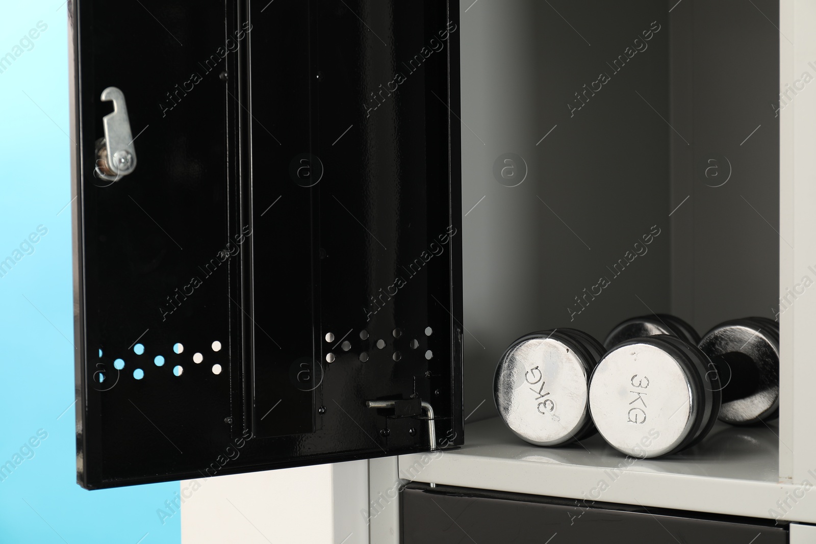 Photo of Open locker with dumbbells on light blue background, closeup