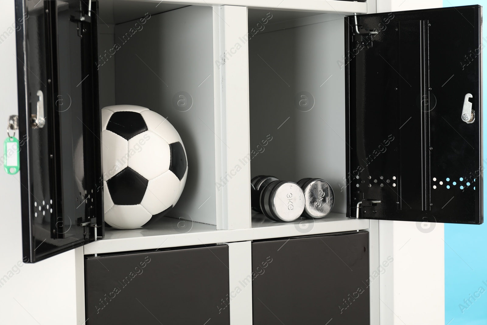 Photo of Open lockers with dumbbells and soccer ball on light blue background, closeup