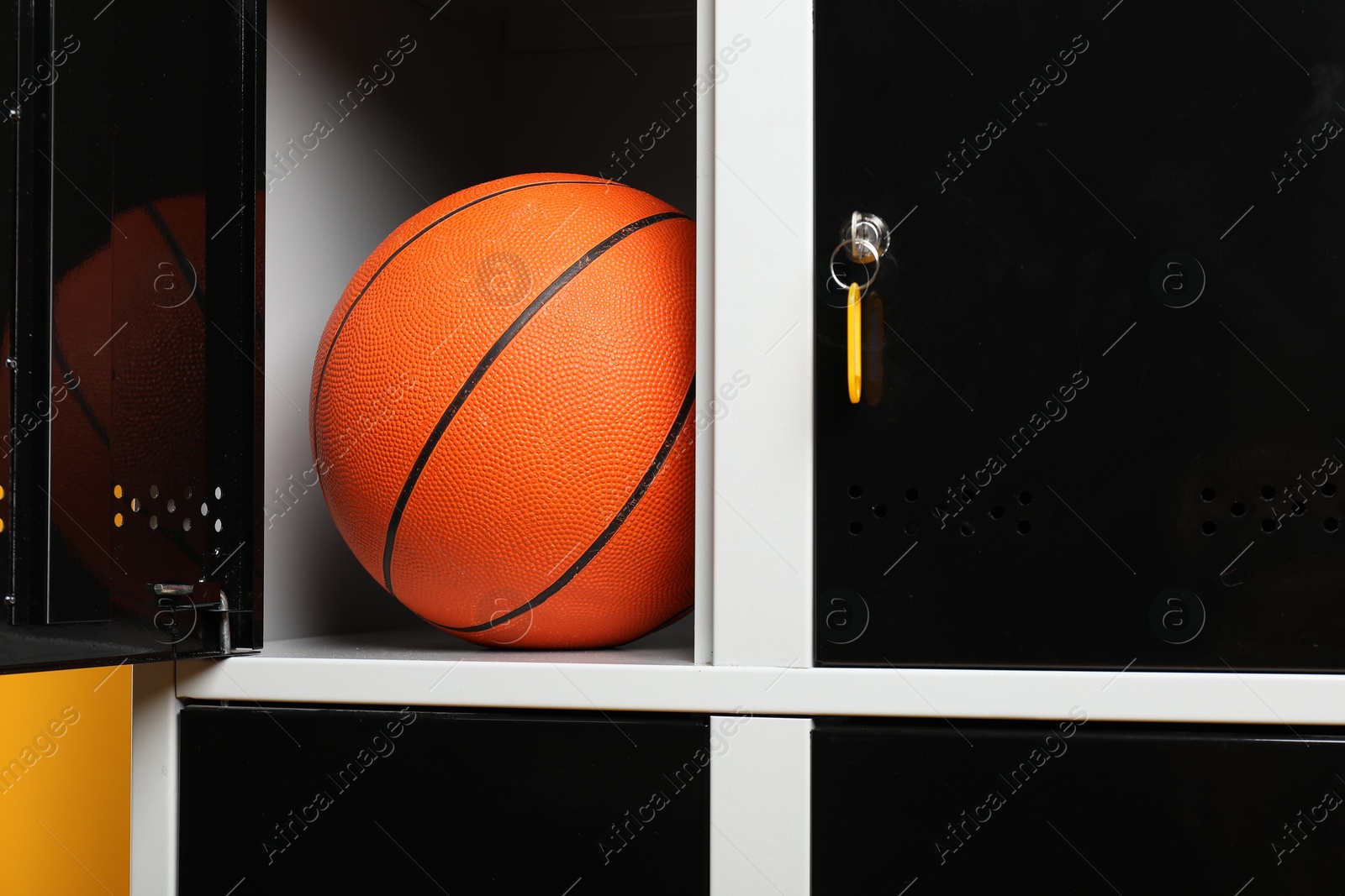 Photo of Open locker with basketball ball on orange background, closeup