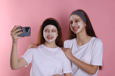 Photo of Teenage girls with masks on their faces and headbands taking selfie against pink background