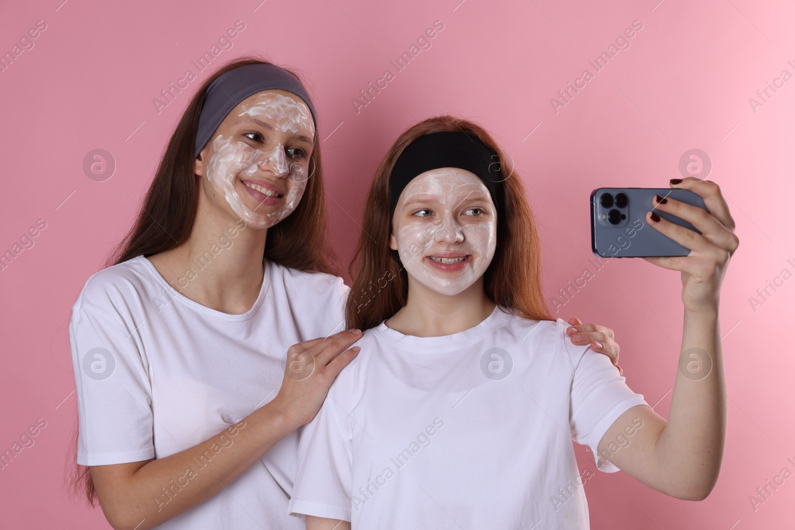 Photo of Teenage girls with masks on their faces and headbands taking selfie against pink background