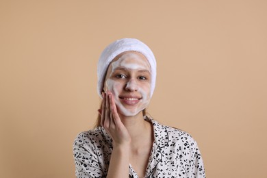 Teenage girl washing her face with cleanser on beige background. Cosmetic product