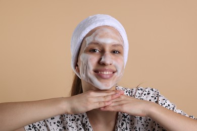 Photo of Teenage girl washing her face with cleanser on beige background. Cosmetic product