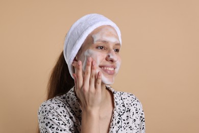 Photo of Teenage girl washing her face with cleanser on beige background. Cosmetic product