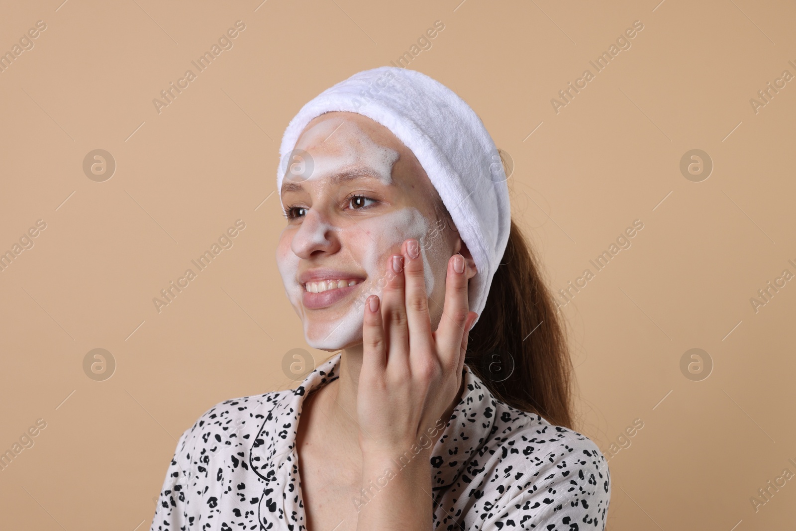 Photo of Teenage girl washing her face with cleanser on beige background. Cosmetic product