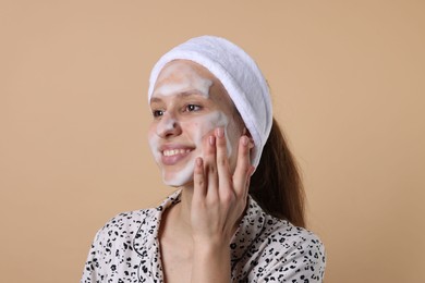 Photo of Teenage girl washing her face with cleanser on beige background. Cosmetic product