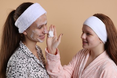 Photo of Teenage girl applying cleansing foam on her friend's face against beige background