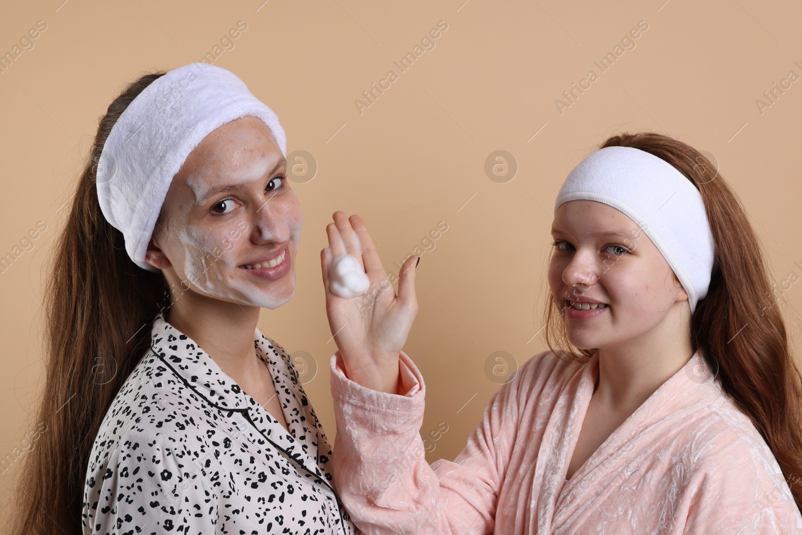 Photo of Teenage girl applying cleansing foam on her friend's face against beige background