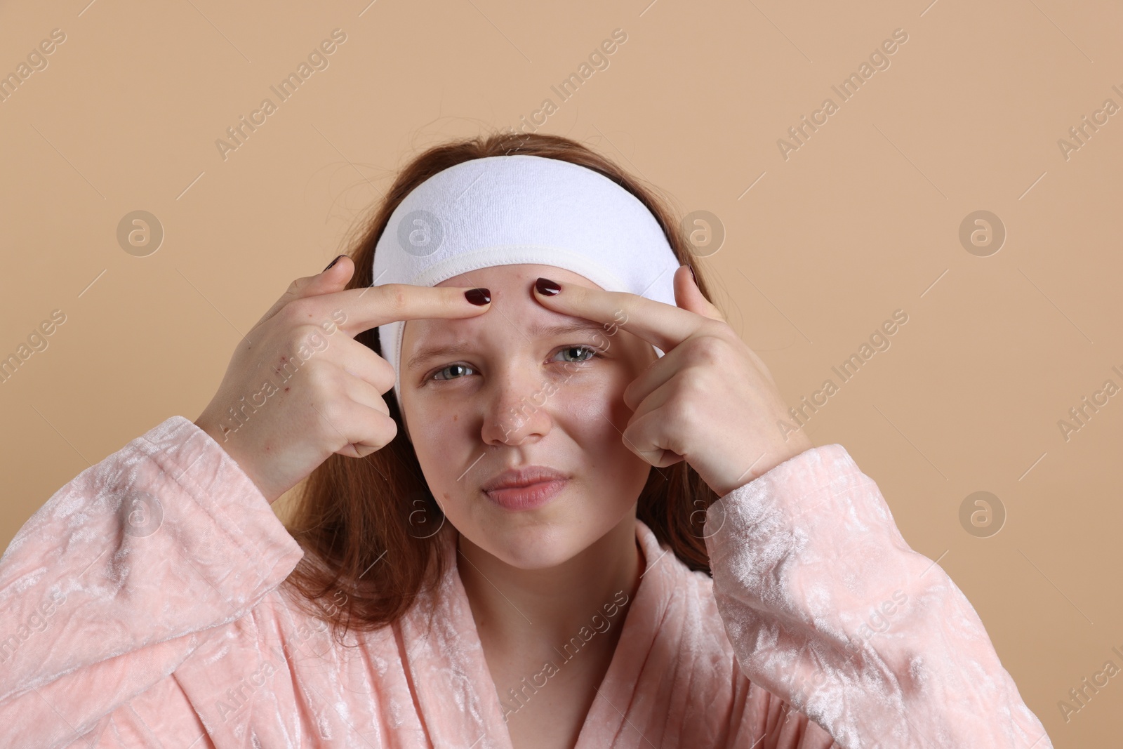 Photo of Teenage girl popping pimple on her face against beige background. Acne problem