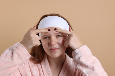 Photo of Teenage girl popping pimple on her face against beige background. Acne problem