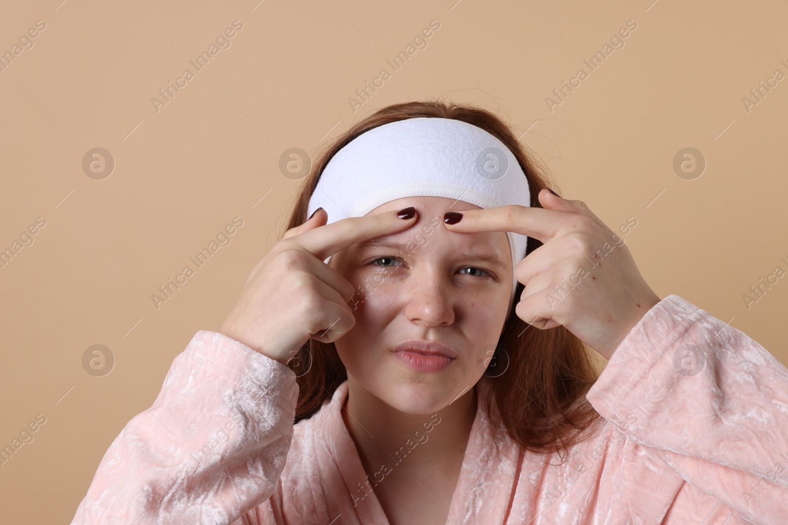 Photo of Teenage girl popping pimple on her face against beige background. Acne problem