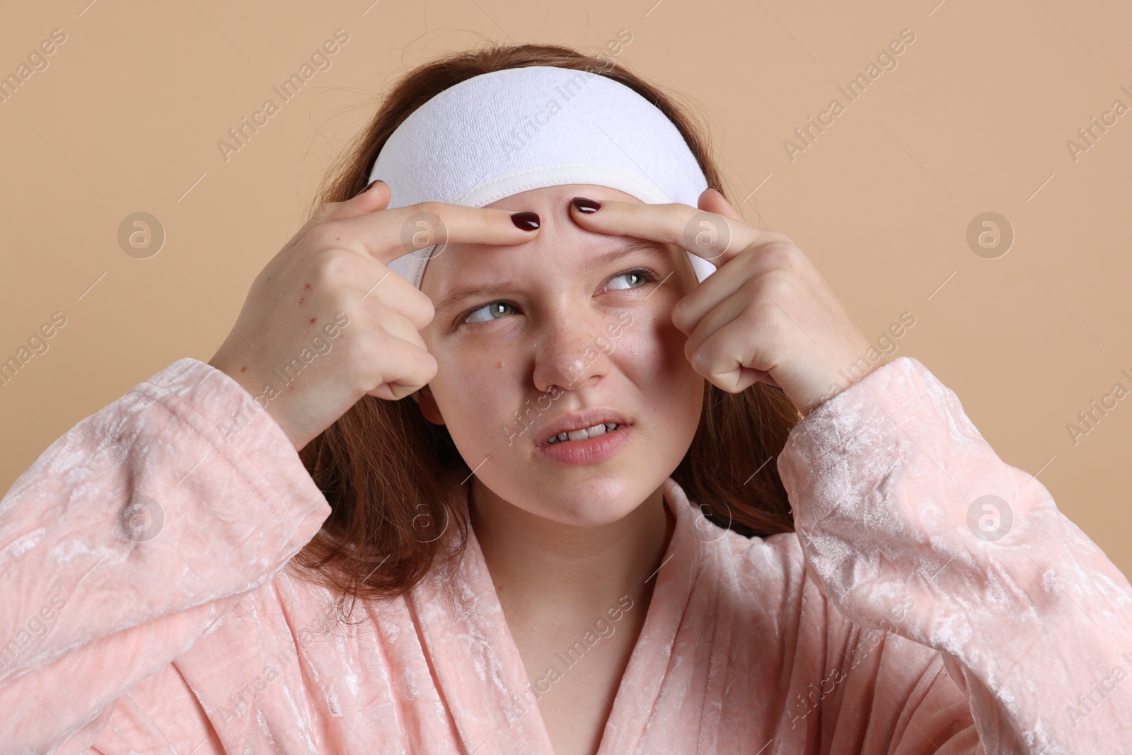 Photo of Teenage girl popping pimple on her face against beige background. Acne problem