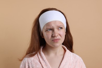 Photo of Upset teenage girl with headband against beige background. Acne problem