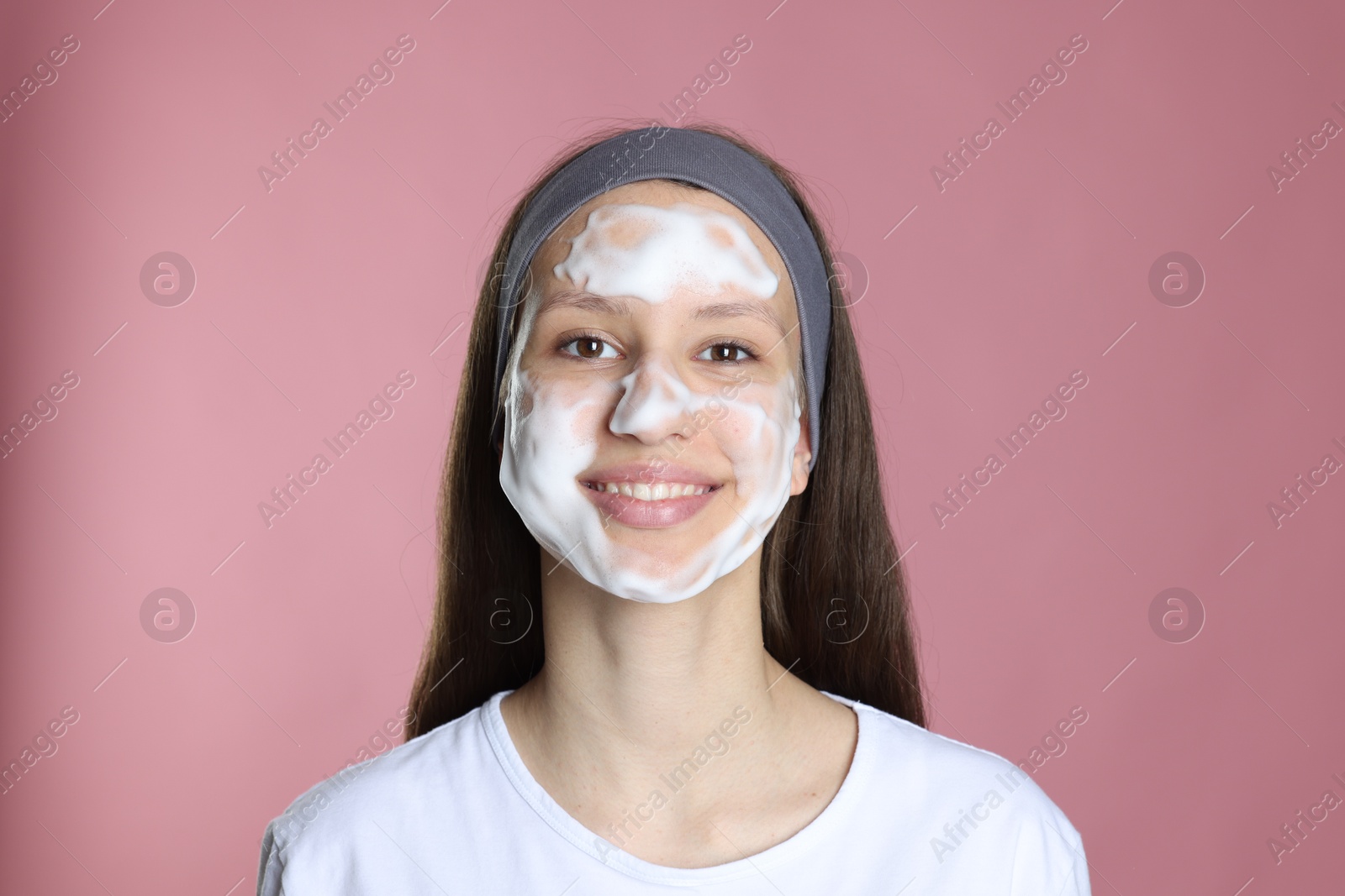 Photo of Teenage girl with cleansing foam on her face against pink background. Acne treatment