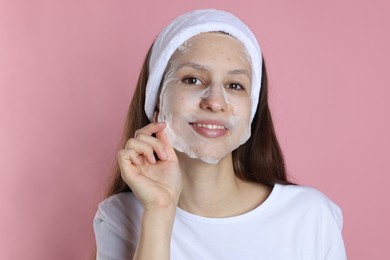 Photo of Teenage girl removing sheet facial mask on pink background. Acne treatment