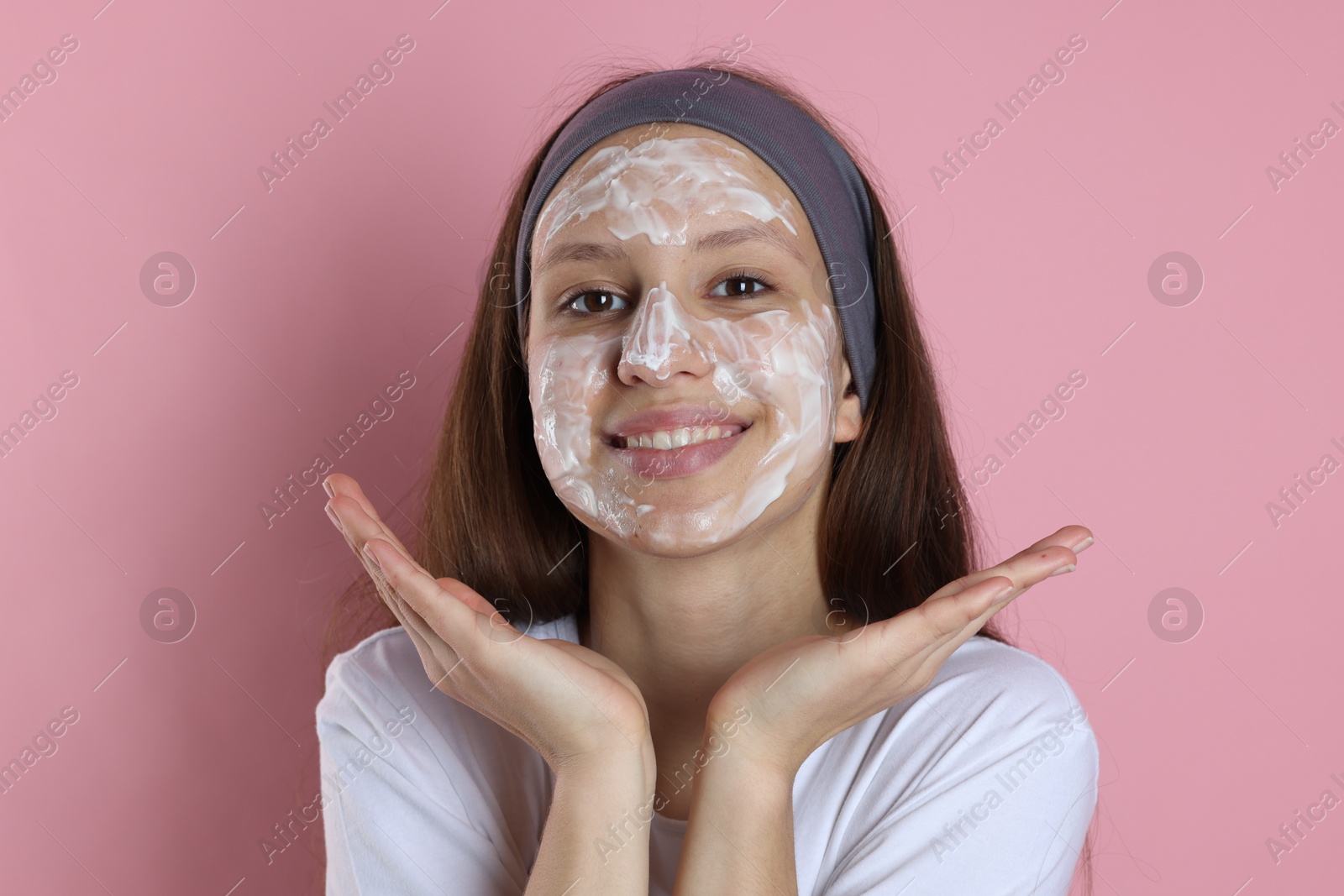 Photo of Teenage girl with cream on her face against pink background. Acne treatment